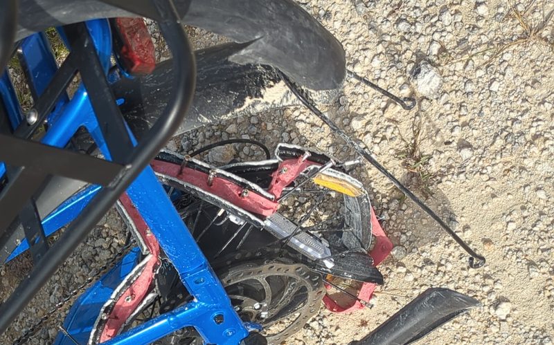 A collapsed e-bike rear wheel with splayed spokes, lying on limestone aggregate.